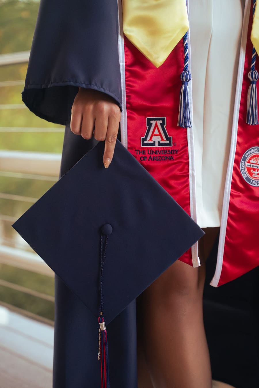 Close-up of a graduate's hand holding a mortarboard against a red stole
