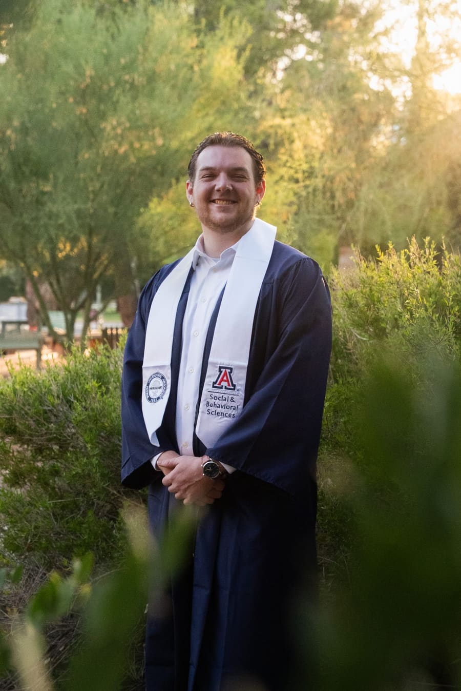 Smiling graduate in navy gown and white stole among desert greenery