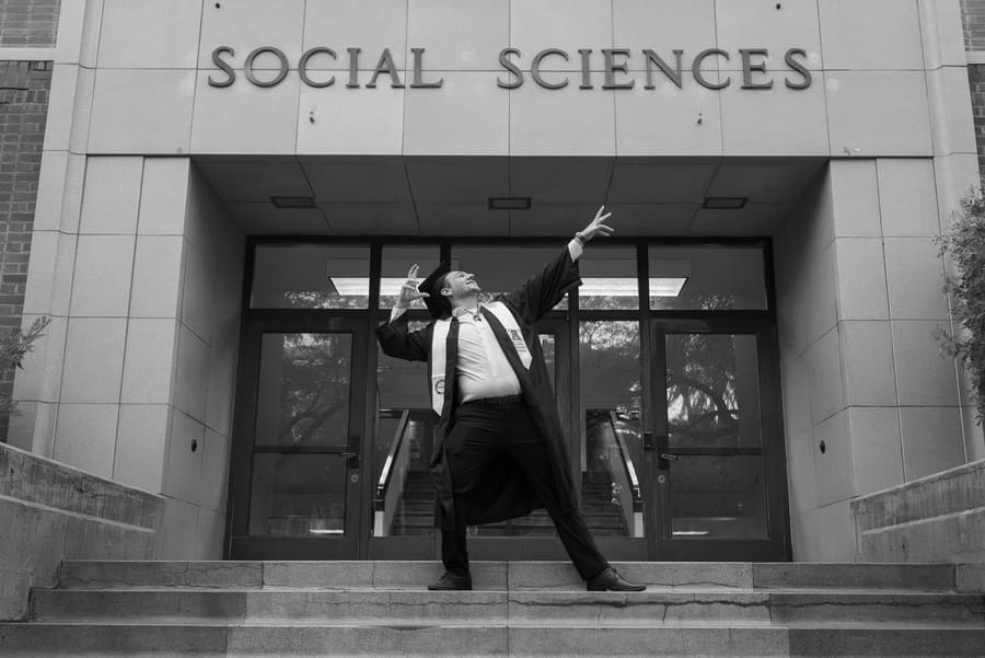 Black-and-white shot of a graduate striking a pose outside the Social Sciences building