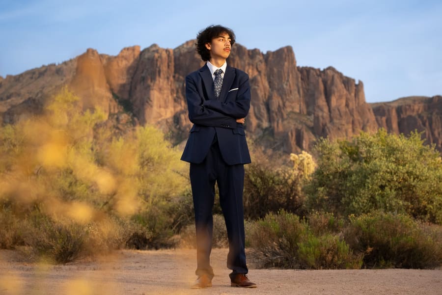 Young man in a navy suit standing before desert cliffs at golden hour