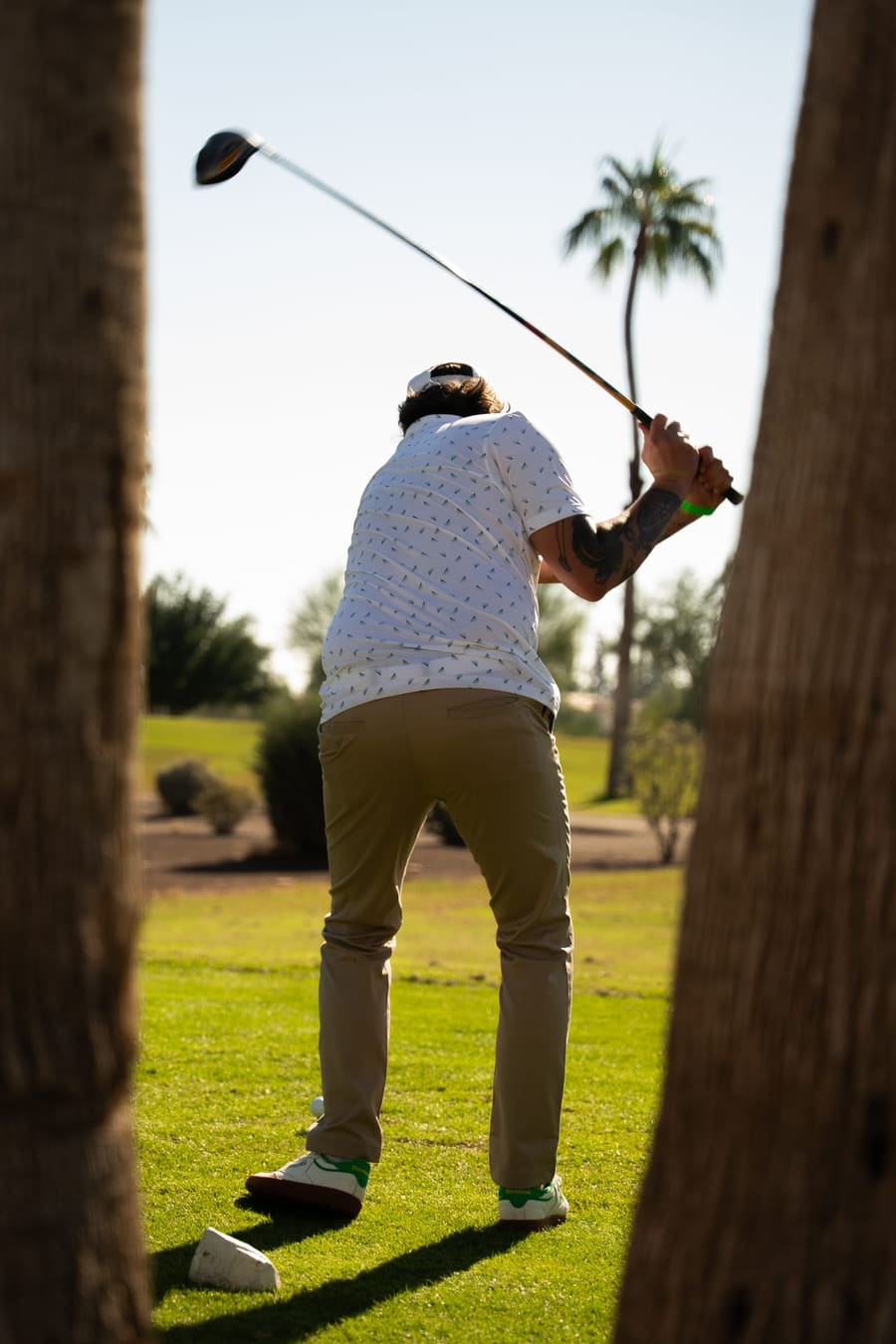 Golfer swinging, framed between two palm trunks